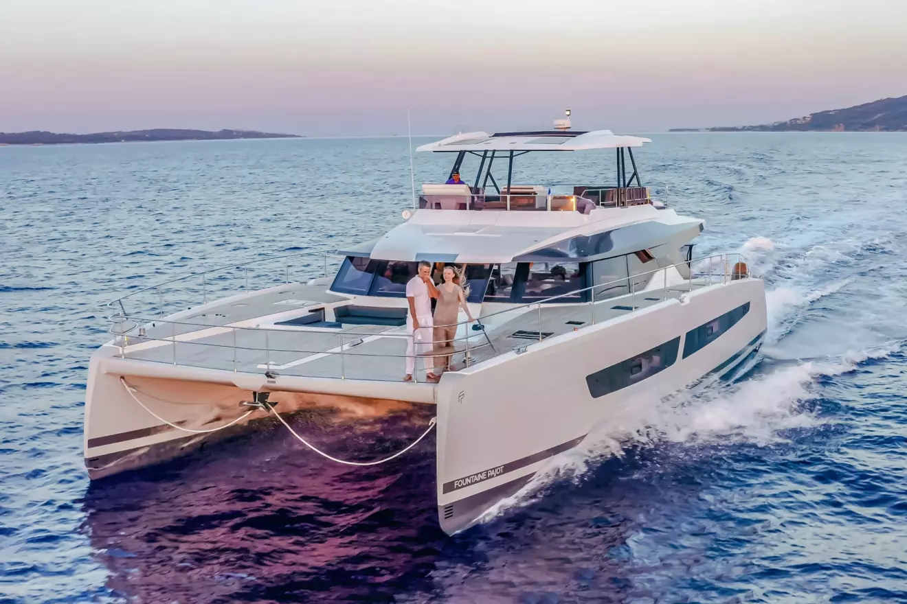 Fountaine Pajot Power 67 power catamaran moving through blue water, with a couple standing on the foredeck. 